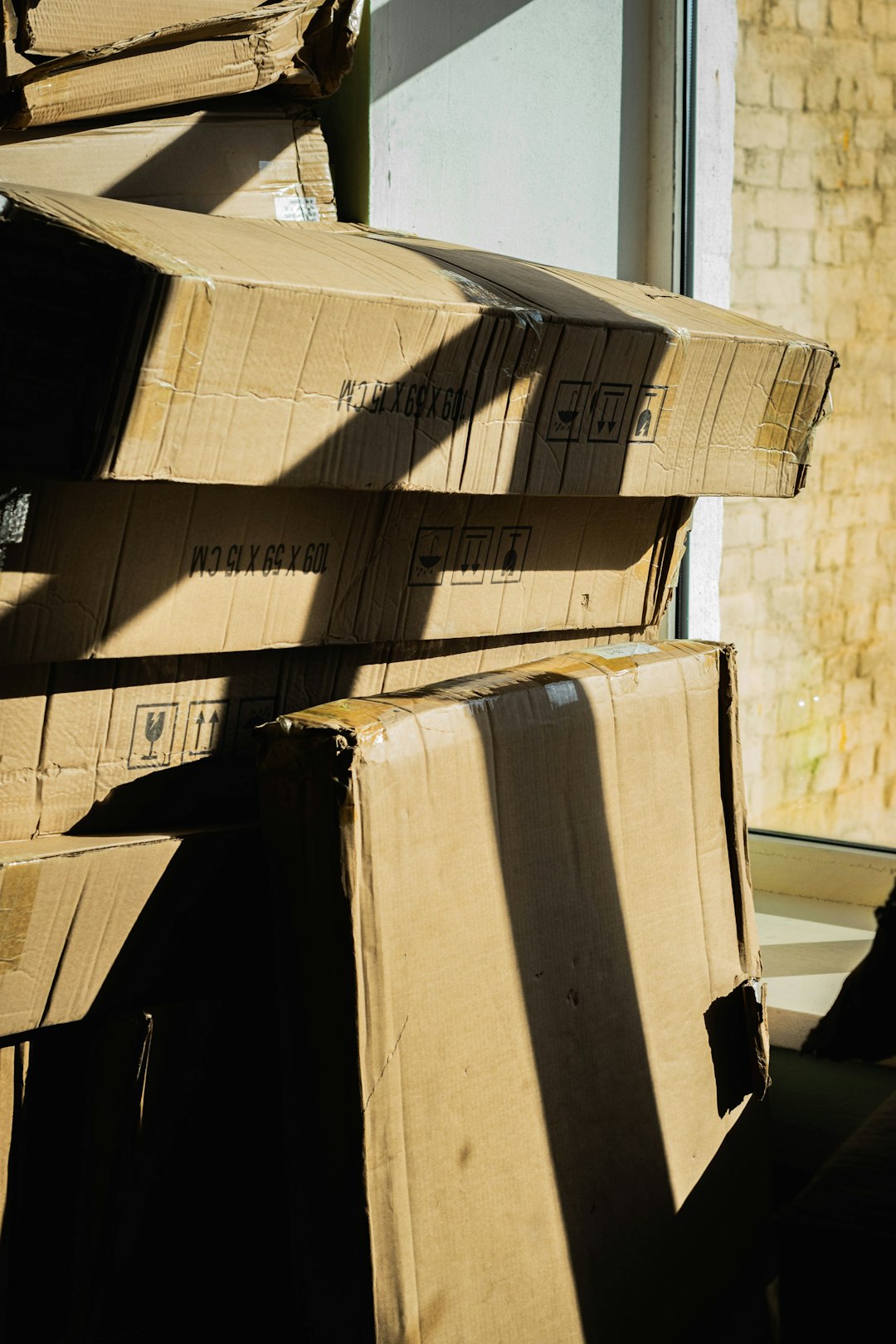 Stack of worn cardboard boxes lit by strong sunlight creating dramatic shadows and textured surfaces.