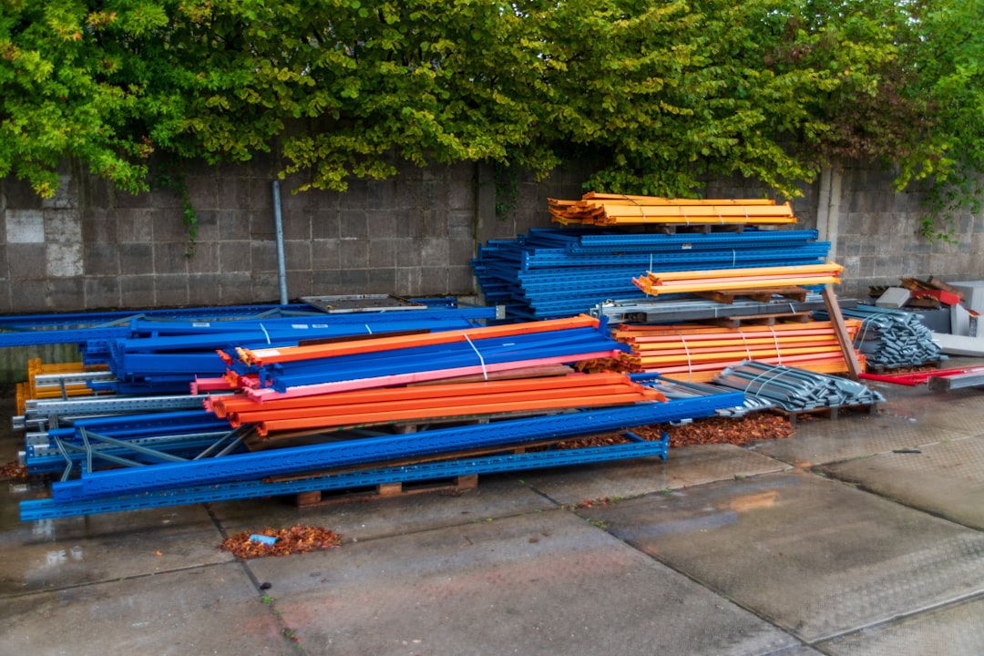 stacks-of-blue-and-orange-industrial-shelving-components-outdoors-6seayahehmi
